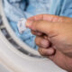 Hand removing lint from fabric trapped on laundry dryer filter