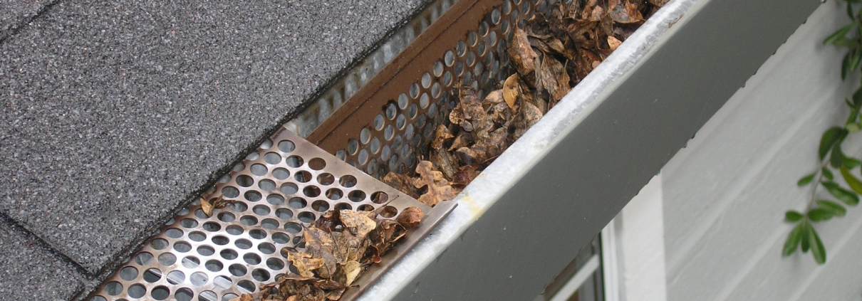 A dirty, clogged gutter causing home problems as a result of not cleaning gutters regularly.